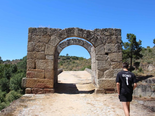 jovem a chegar à torre de entrada de uma ponte em granito